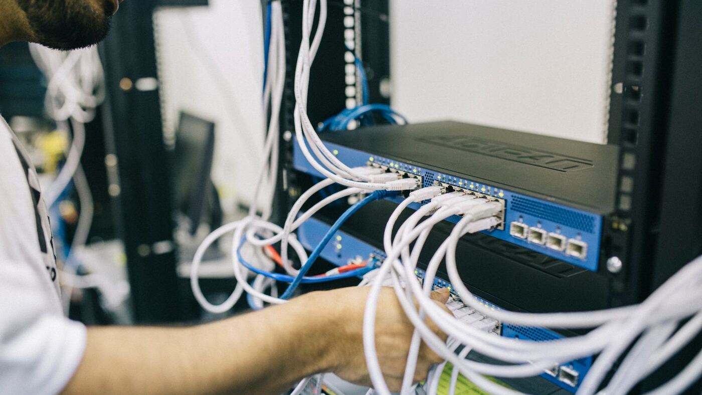 Technician’s hand working white ethernet cables into blue rack-mounted network switches with active status lights