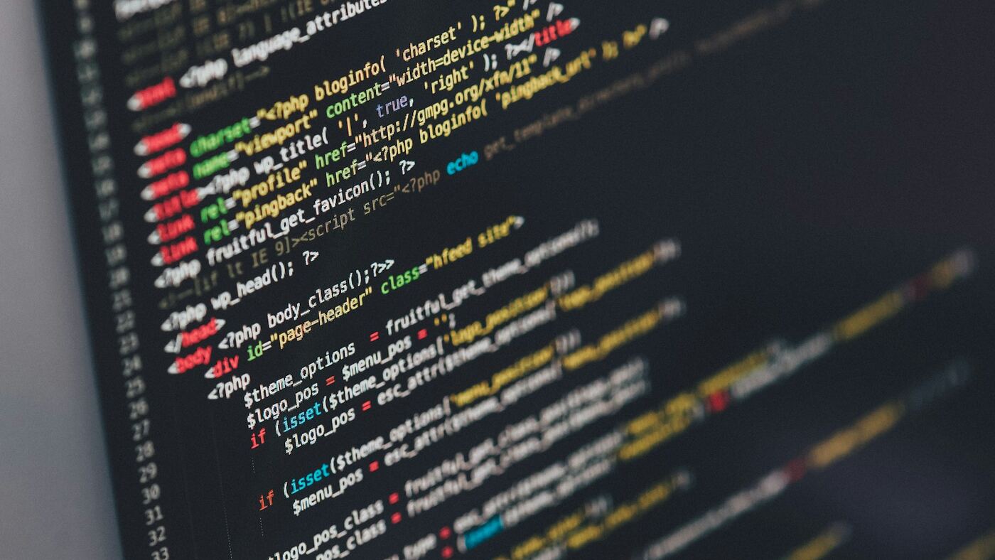 Angled close-up of a dark-themed code editor with syntax-highlighted HTML and PHP on a developer workstation