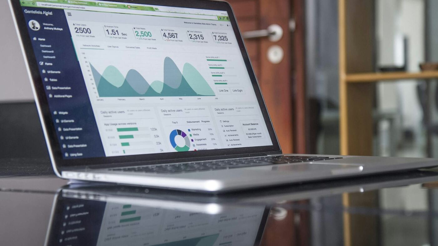 Silver laptop on a reflective desk displaying a polished analytics dashboard with charts and performance metrics